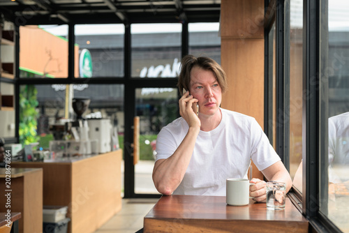 Bilde på lerret Serious Scandinavian man talking on phone in cafe horizontal format