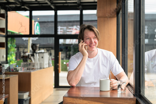 Bild auf Leinwand Smiling Scandinavian man talking on phone in cafe horizontal format