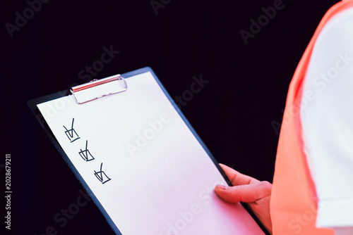Worker in safety vest views clipboard with checkmarks from side.