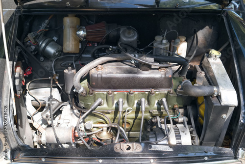 Mechanics work on an engine inside a classic car under the hood on a sunny day in a garage