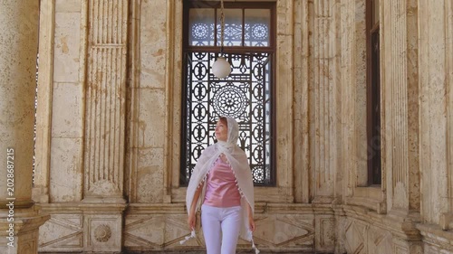Slow motion shot of female traveler walking toward camera inside historic mosque corridor in Cairo, Egypt. Elegant Islamic architecture and ornate marble details in cinematic 4K travel footage.