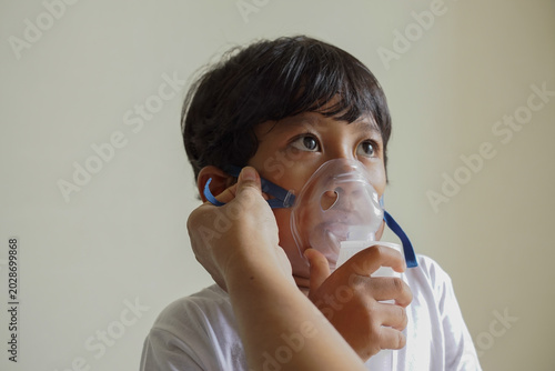 Fotografía Close up young child receiving respiratory treatment, person hand helping to wearing mask, focus on eyes and unwell face expression