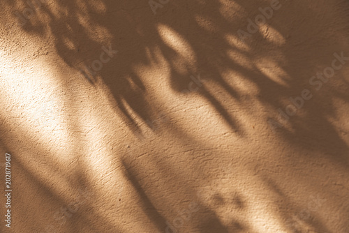 Obraz na płótnie Dappled sunlight through leaves creates a soft pattern on an ochre plaster wall