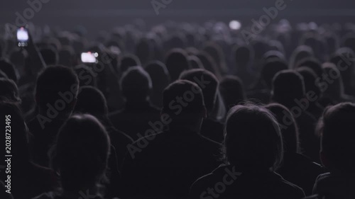 Audience silhouettes seated in dark cinema hall, watching film projection. Mood quiet, anticipatory, cinematic, communal experience.