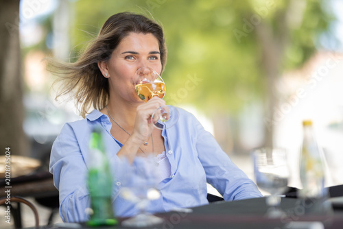 Photos Woman enjoys drink at outdoor cafe on a sunny day while sitting at a table with