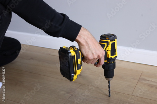 Foto Hand using cordless drill on wooden floor indoors, rechargeable power tool for D