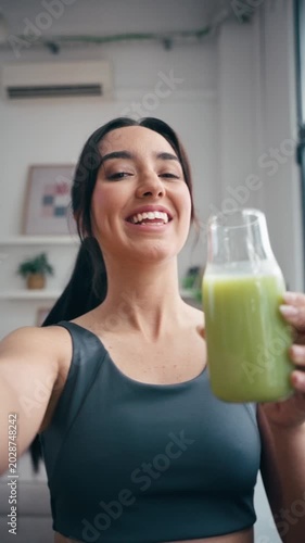 Video of itness woman drinking a healthy green juice while taking a selfie with smartphone in the kitchen at home