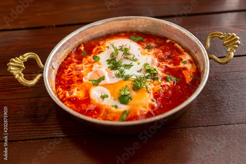 hot fresh shakshuka with garlic and herbs in a small frying pan on a wooden table