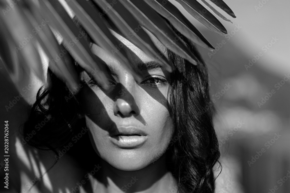 Obraz premium Black and white portrait with palm leaf shadow. Monochrome beauty face with dramatic light and contrast. Closeup woman portrait with strong shadow pattern. Fashion beauty summer face.
