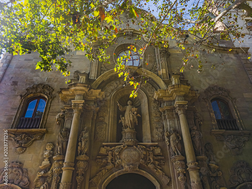 Manresa, Spain - October 1, 2025: Ornate facade of the Sanctuary of the Cave of Saint Ignatius in Manresa, Catalonia, Spain. Historic religious architecture with sculptural details framed by green tre