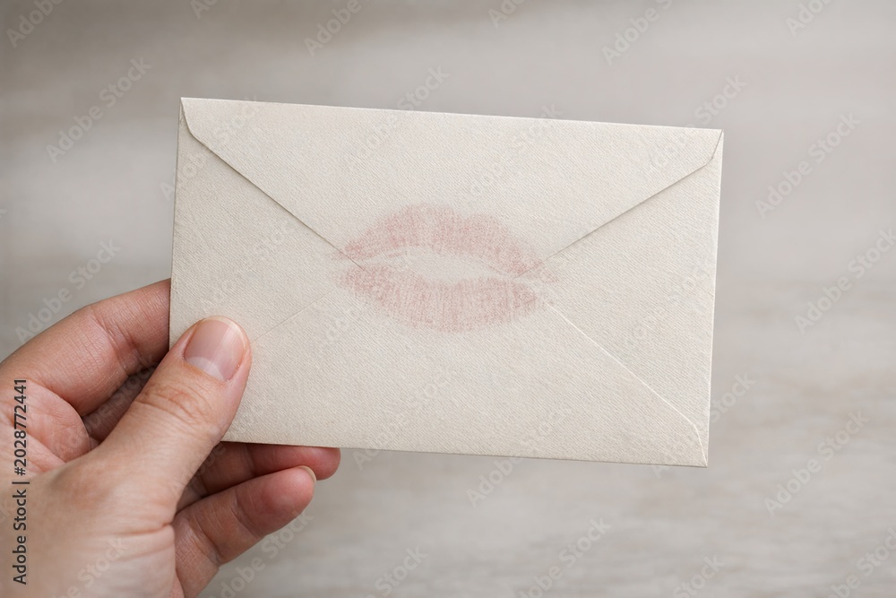 Fototapeta premium A person holds a white envelope with a bold red lipstick imprint, suitable for use in scenes about secrecy, surprise, or intimate moments