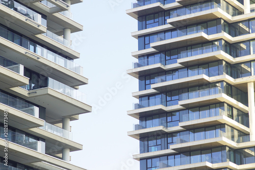 Close-up of two glass-balcony residential towers facing each other across narrow sky gap. Conveys vertical urban density, speculative apartment development, and contemporary city expansion.