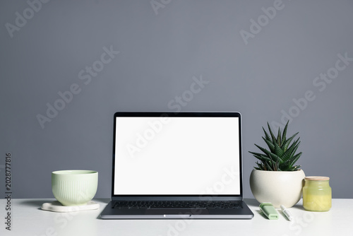 Stylish workplace. Laptop with blank screen, cup and decor on white table against gray background. Space for text