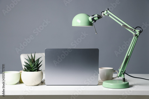 Stylish workplace. Laptop, lamp, cup and decor on white table against gray background