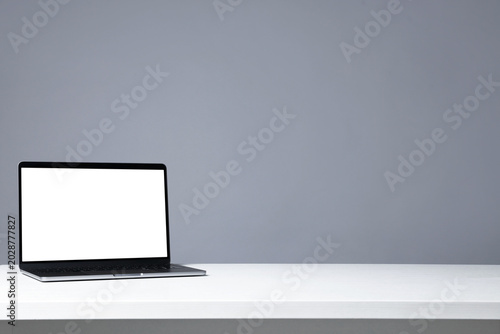 Stylish workplace. Laptop with blank screen on white table against gray background. Space for text