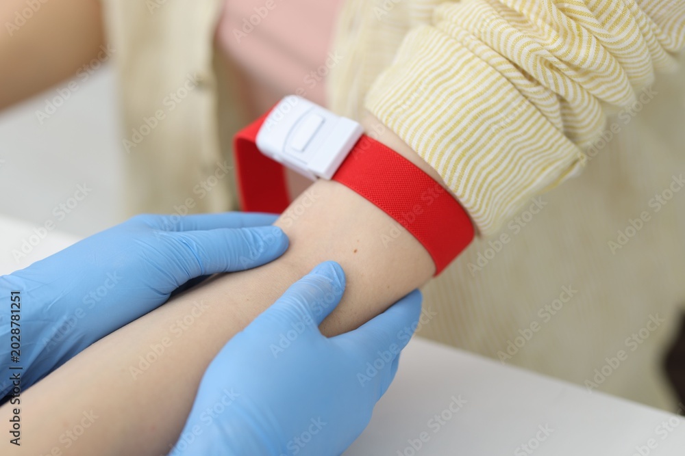 Obraz premium Nurse palpating patient's vein before drawing blood sample at white table in clinic, closeup