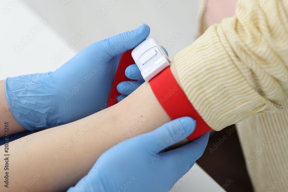 Obraz premium Nurse putting medical tourniquet on patient's arm in clinic, closeup