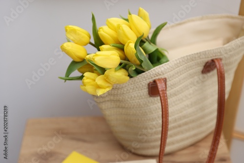 Yellow tulips in wicker bag on wooden chair indoors, closeup