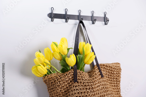 Yellow tulips in wicker bag hanging on white wall, closeup
