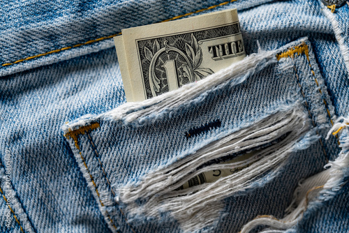 One dollar bill in ripped blue jeans pocket. Closeup of a folded US dollar banknote sticking out of a torn denim pocket. Financial crisis, poverty, and budget concept