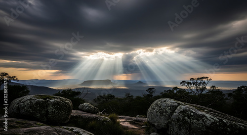 Dramatic Sun Rays Breaking through Clouds over Rocky Landscape