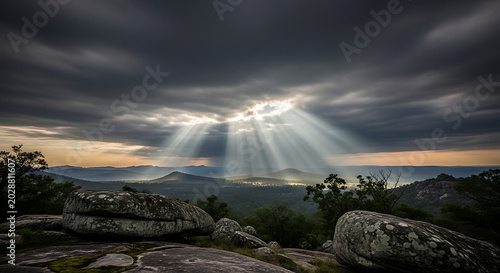 Dramatic Sun Rays Breaking through Dark Clouds over Rocky Mountain Landscape