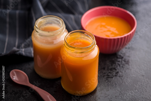 Homemade Baby Food Carrot Puree in Glass Jars with Bowl and Spoon on Dark Surface