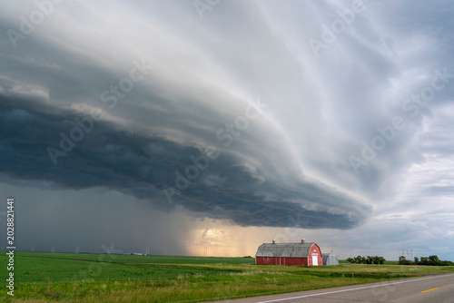 Dramatic shelf cloud looms over a red barn and green fields under a stormy sky