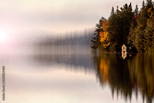 Bild auf Leinwand Serene cabin nestled among autumn trees reflected in a misty lake