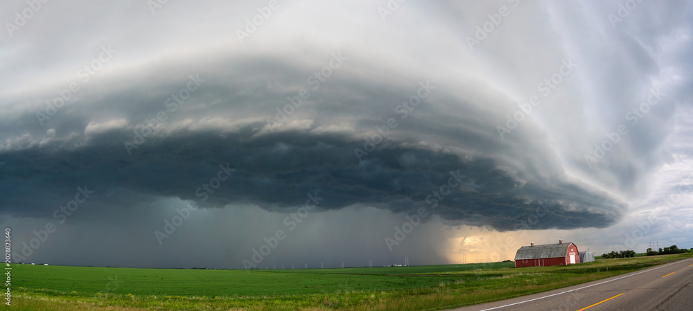 Fototapeta premium Massive supercell thunderstorm looms over a rural landscape with a red barn