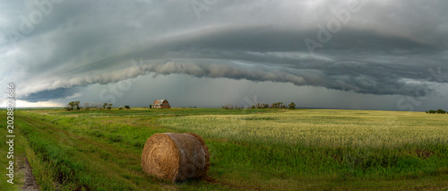 Dramatic storm clouds loom over a rural landscape with a barn and hay bale