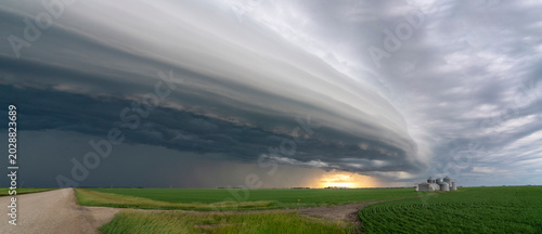 Dramatic shelf cloud formation over a rural landscape with grain silos