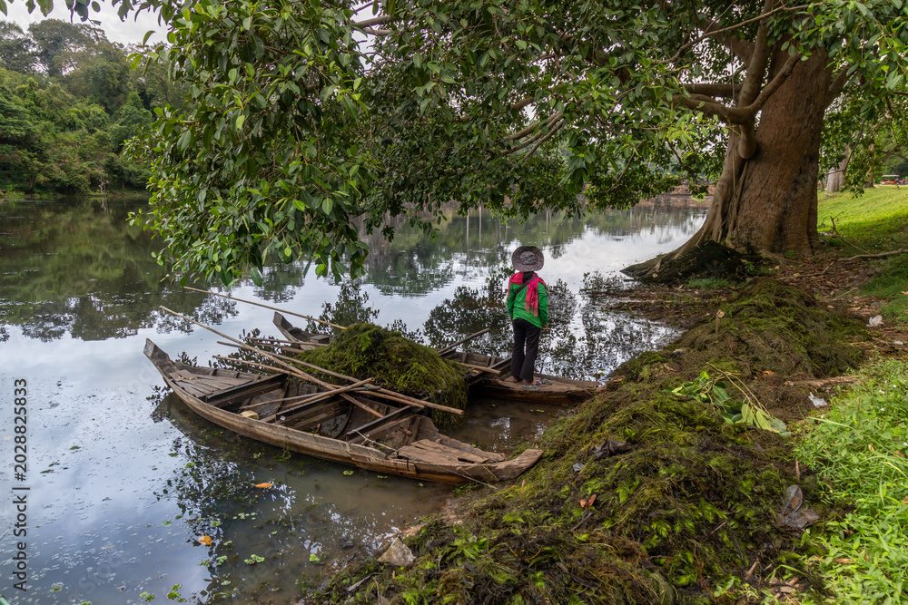 Fototapeta premium Women in boats in Ankor Wat clean up aquatic plants from a lake surrounded by lush jungle vegetation. Siem Rep, Cambodia