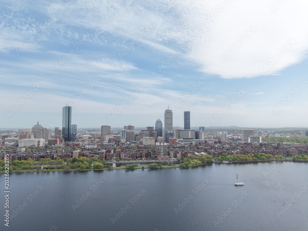 Obraz premium Aerial drone view of the Boston skyline under a cloudy sky, featuring the Charles River, Harvard Bridge, and Back Bay brownstones leading toward the Prudential and John Hancock towers.
