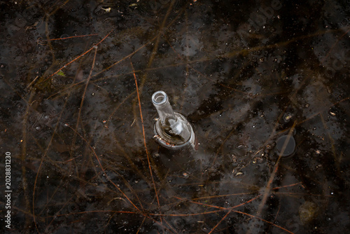 Quadro su tela Glass bottle floating in polluted murky water
