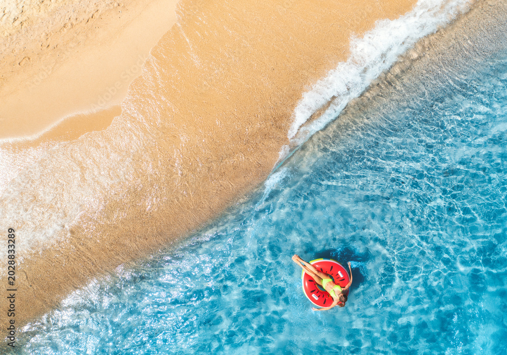 Obraz premium Aerial view of a young woman swimming with red swim ring in blue sea with waves in summer. Tropical landscape with girl, clear water, sandy beach. Top down view. Vacation. Sardinia island, Italy