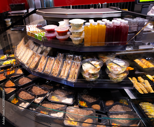 Supermarket display with packaged ready meals, sandwiches, salads, and juices. Convenient takeaway food section in grocery store.