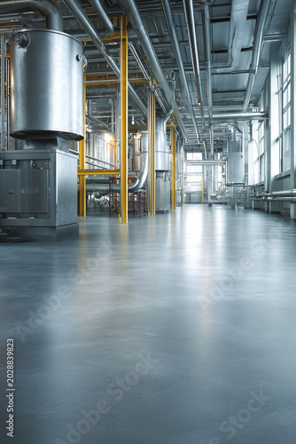 Interior of a modern clean factory floor with shiny gray epoxy ground. Industrial facility with steel pipelines, massive tanks and metal equipment in soft bright daylight