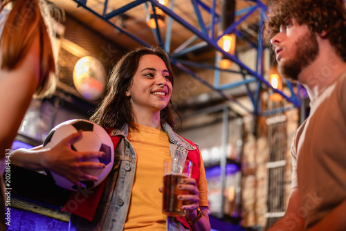 Fotografija Friends holding a soccer ball and talking at a pub bar counter during halftime