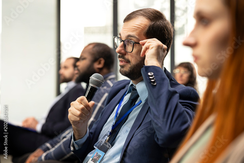 Foto Seated businessman takes microphone to ask questions and engage in debate, interacting with speaker and participants during conference