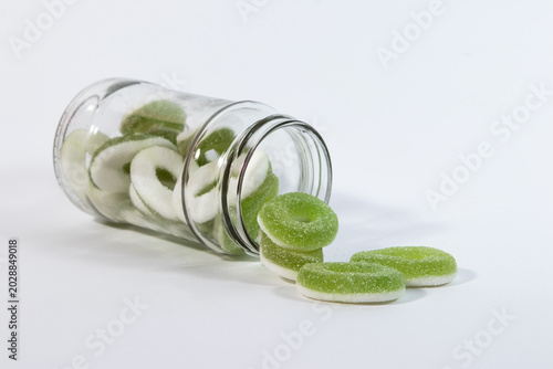 Green and white gummy loop candies spilled out from an open glass jar scattered on a clean white background