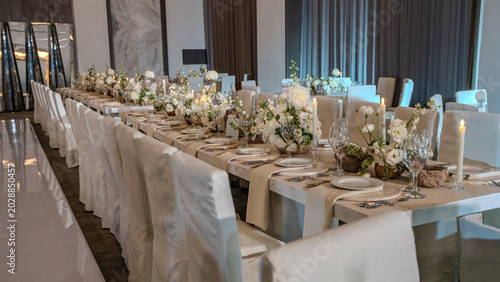 Elegant wedding reception table setting with white floral centerpieces, candles and stone chargers. Luxury banquet dinner decor at wedding venue.