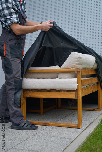 Canvastavla Man removes protective cover from outdoor sofa with cushions on patio