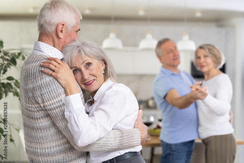 Fototapeta premium Two married couples enjoying slow dancing at a house party for friends