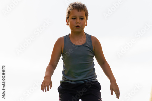 Billede på lærred Young boy jumps with joy in a sunny outdoor setting during playtime