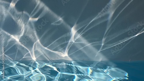 Water reflection creates an abstract light pattern on a textured wall, showcasing blue ripples and caustics. This serene liquid surface movement provides a tranquil and clean background, commercial pr