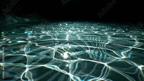 Water surface reflection and light refraction create an abstract background with shimmering caustic patterns on dark water. This fluid motion texture is commercial advertising, graphic design, or as a