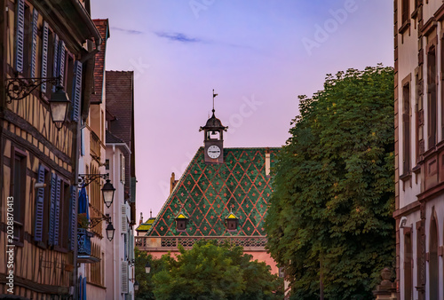 Historic Koifhus old customs building with a distinctive green and red geometric patterned tile roof with a clock tower in Colmar, France at sunset