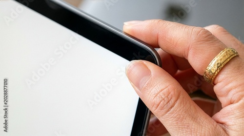 Schilderij op canvas A detailed macro photograph of a person's hand with a gold ring gripping the bezel corner of a modern digital tablet mockup with a blank white screen