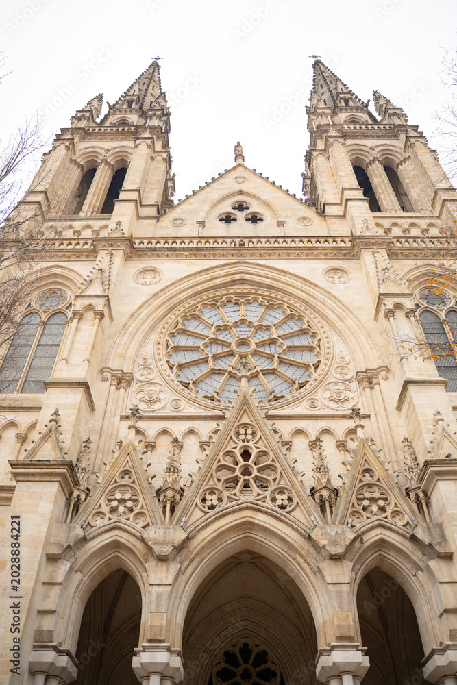 Fototapeta premium Symmetric vertical view of gothic cathedral facade. Ancient neo-gothic church with stone rose window and towers. Epic historic architecture background in Bordeaux, France. 